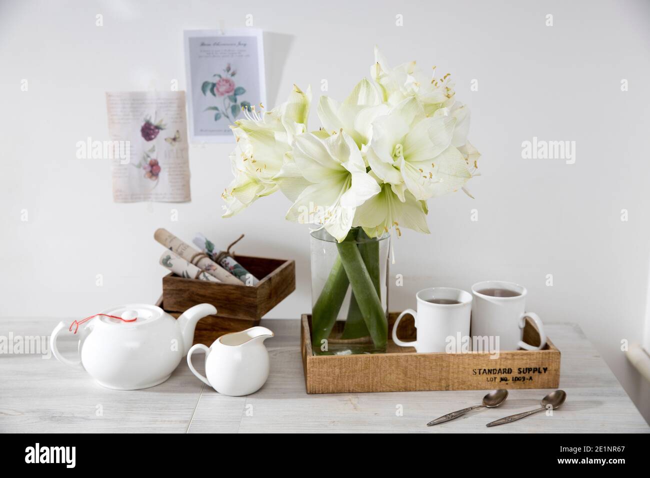 Mosca, Russia - 25 dicembre 2020, un bouquet di giglio bianco in vaso di vetro su un tavolo con due tazze alte di caffè, una teiera, cucchiai e una caraffa di latte. Foto Stock