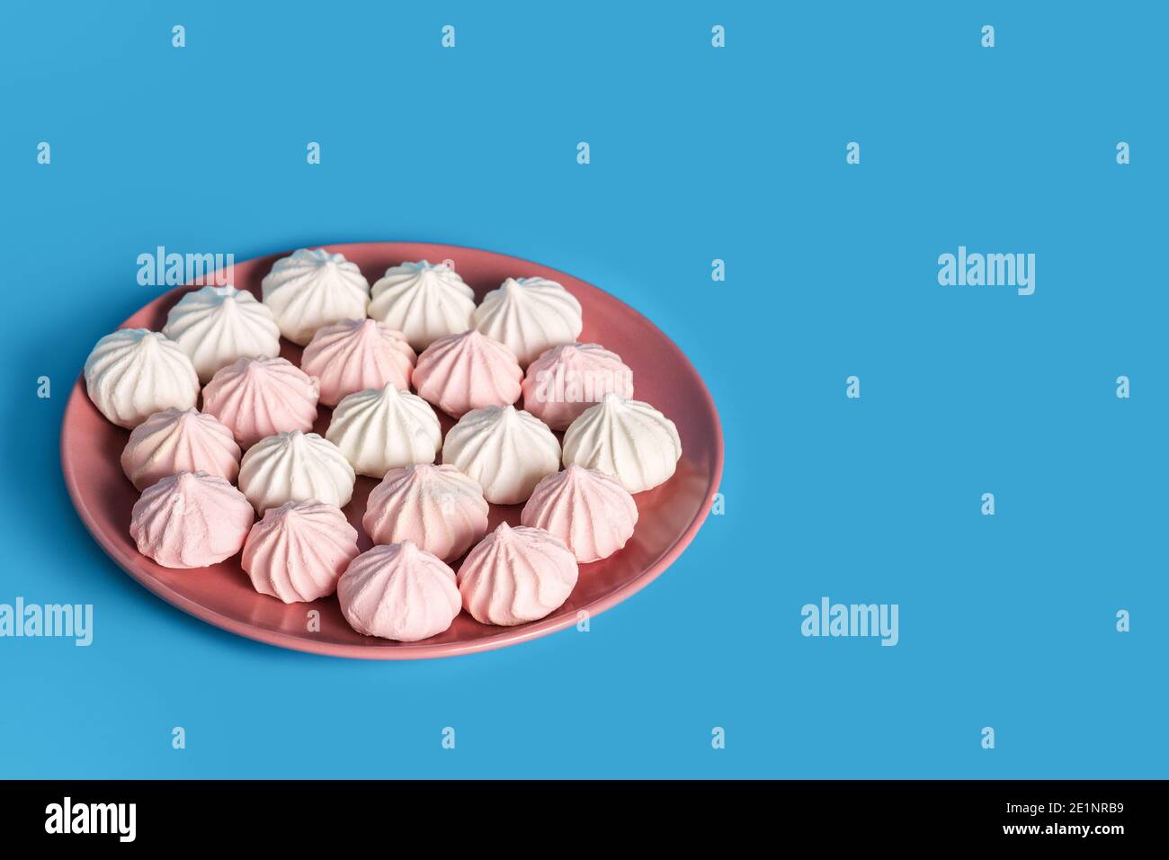 Dessert di proteine dello zucchero in colori pastello in un piatto rosa su sfondo blu. Copia spazio Foto Stock