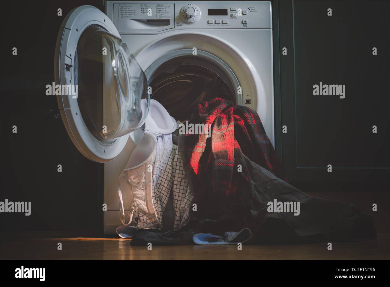 Gli oggetti di abbigliamento non lavati fuoriescono da una lavatrice aperta sul pavimento. Foto Stock