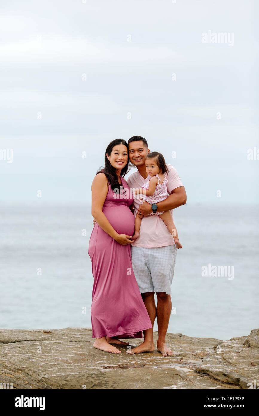 Trasmissione via IR di papà asiatico, bambino e moglie molto incinta sulle rocce dall'oceano Foto Stock
