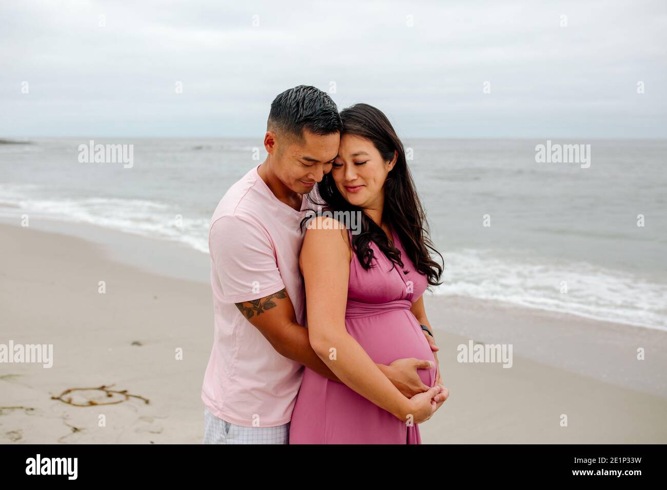 Il marito amorevole abbraccia la moglie incinta da dietro all'oceano Foto Stock