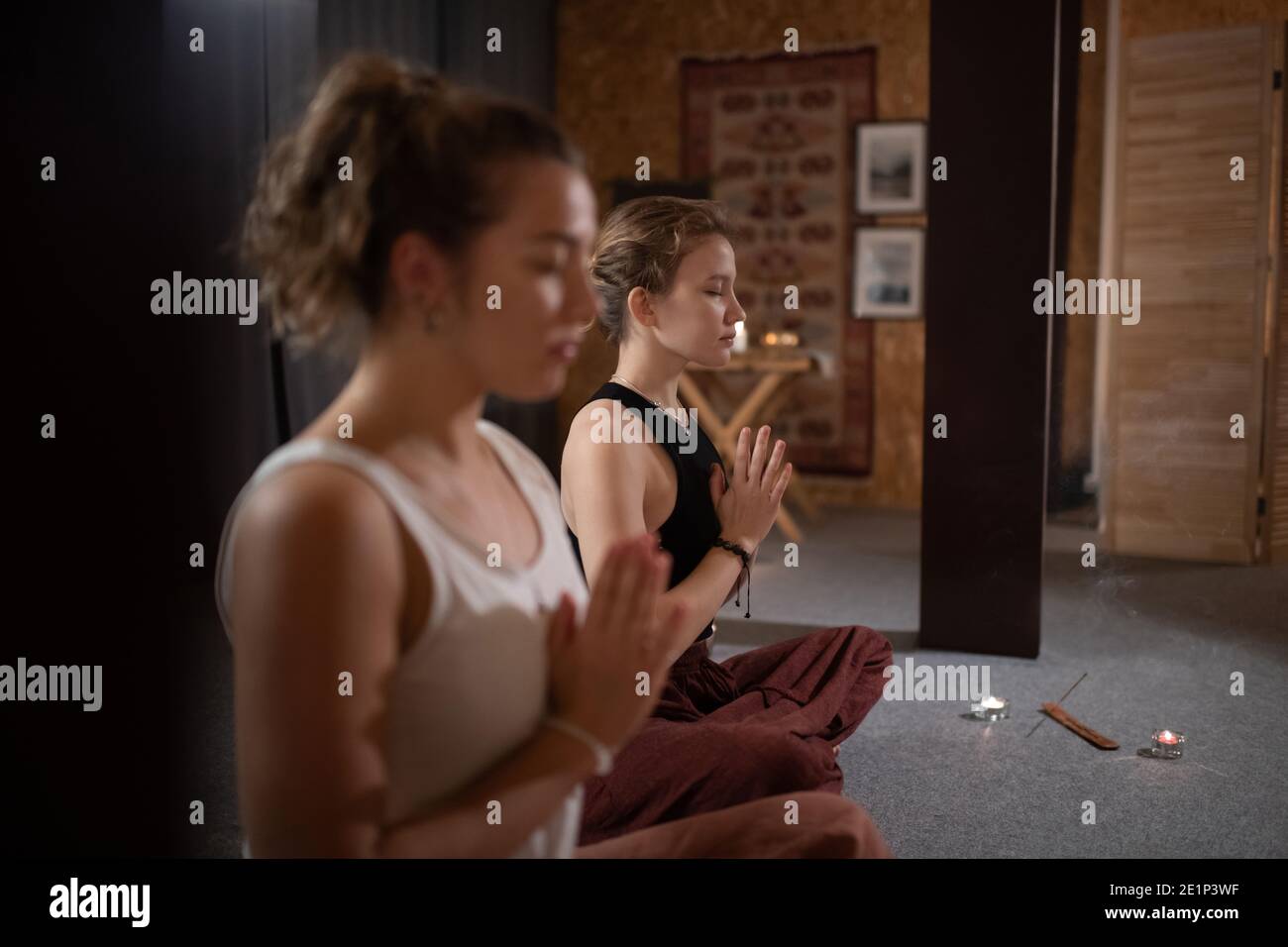 Giovane femmina che si aggrappano le mani e medita con la vettura durante lo yoga lezione in studio Foto Stock