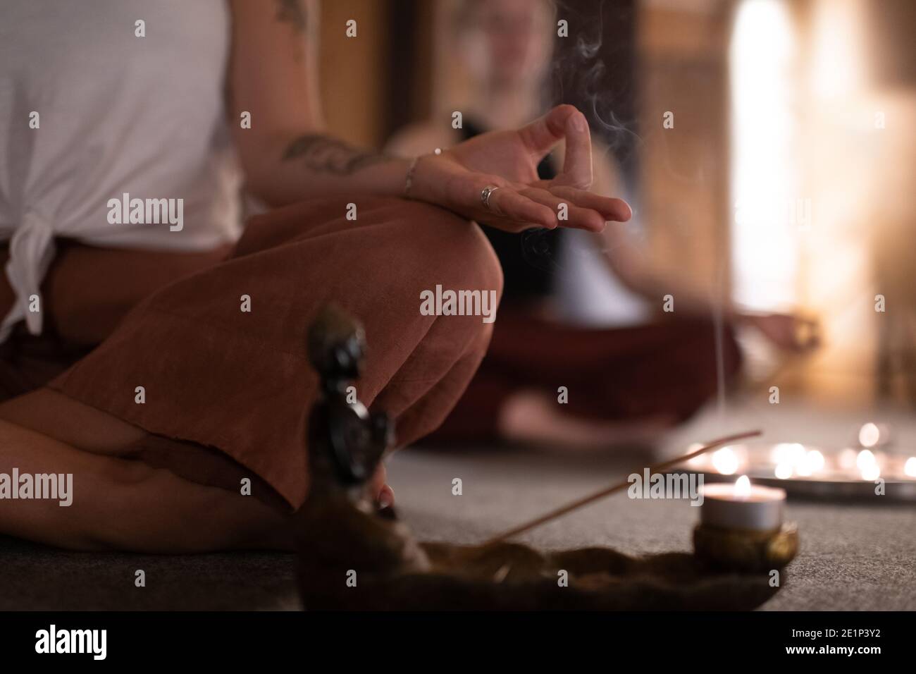 Donna groppata gesturing Gyan mudra e meditating vicino incenso bruciante in studio Foto Stock