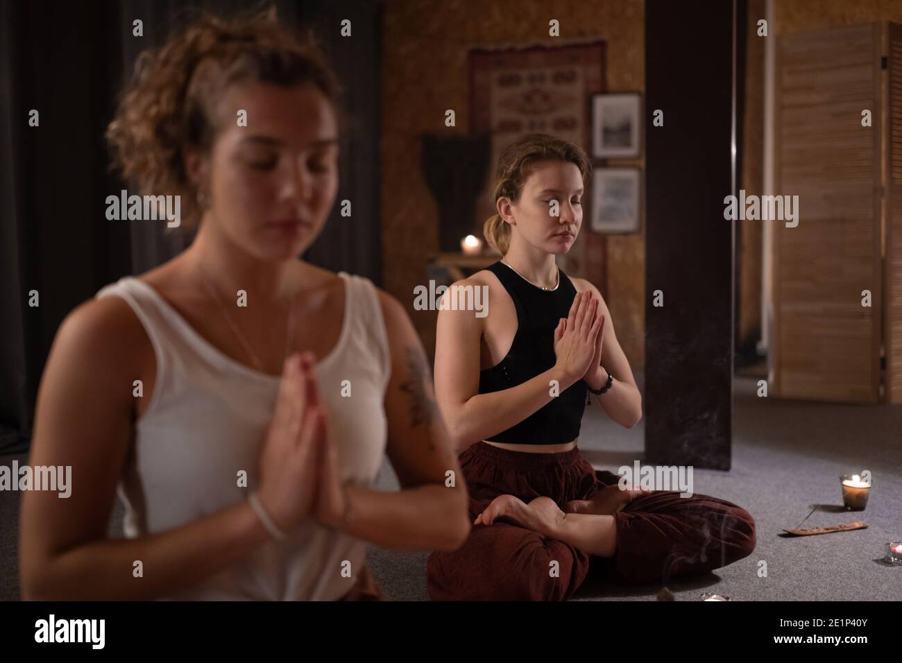 Giovane femmina che si aggrappano le mani e chiude gli occhi con l'amico dentro studio di yoga scuro Foto Stock
