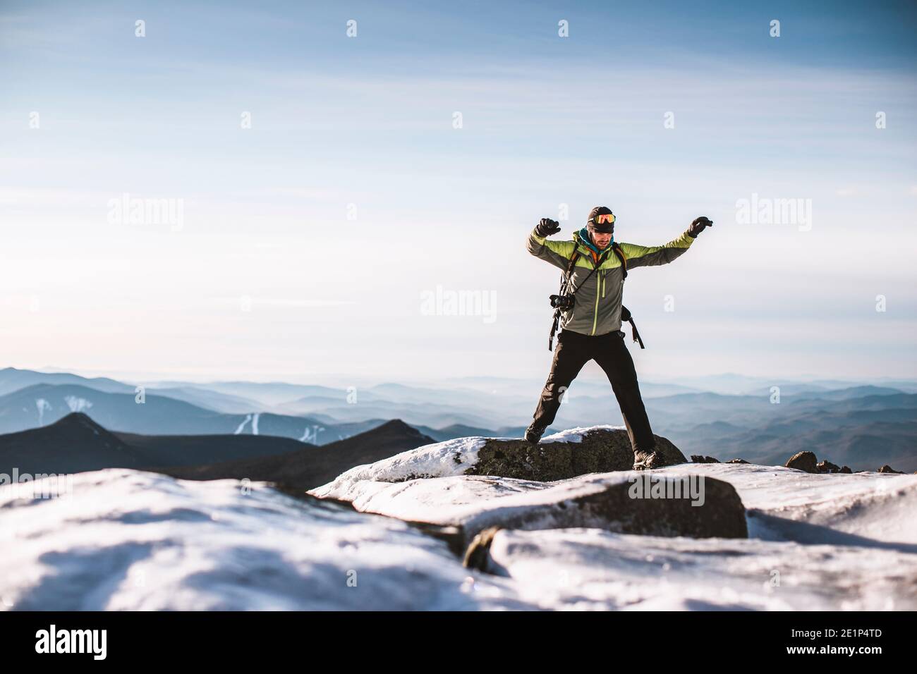 L'uomo con la macchina fotografica salta dalla roccia ghiacciata sulla cima della montagna in inverno Foto Stock