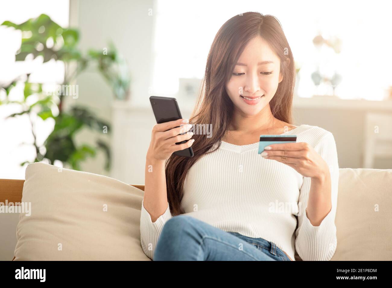 giovane donna che acquista online con carta di credito e smartphone seduto sul divano a casa Foto Stock