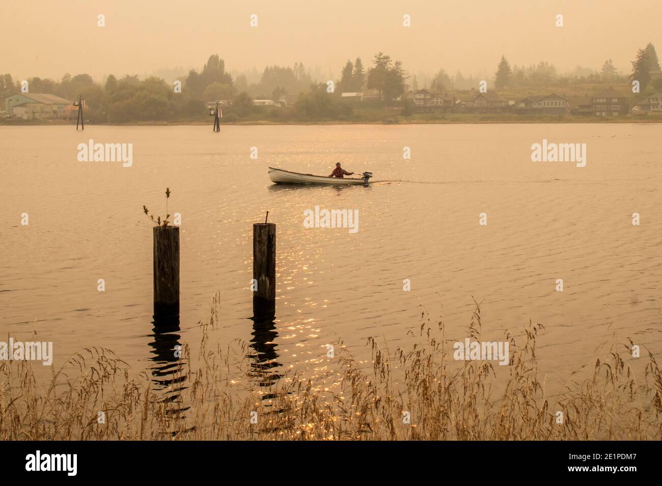 Pescatore nella sua barca Tyee sull'estuario del fiume Campbell, con cielo fumoso proveniente dai fuochi selvatici della California nel 2020. Il sole e il fumo hanno reso il colore roseo. Foto Stock