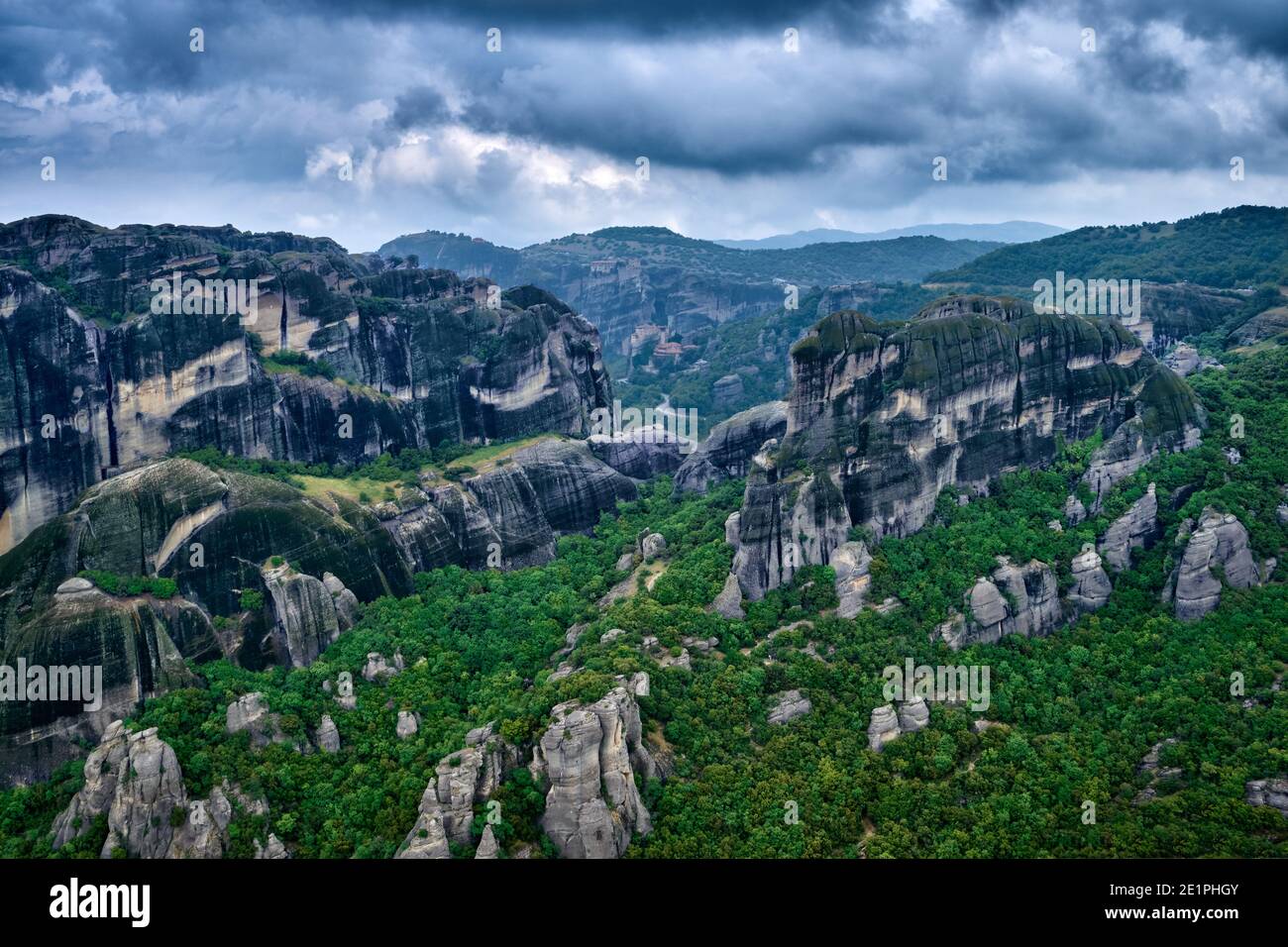 Vista su imponenti colonne di rocce sedimentarie nell'iconica valle di Meteora in nuvoloso giorno di primavera. Colline coperte di alberi, strade tortuose, Grecia Foto Stock