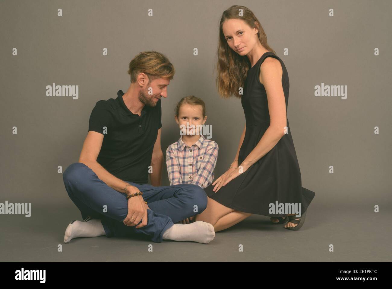 Giovane famiglia felice legare insieme contro lo sfondo grigio Foto Stock