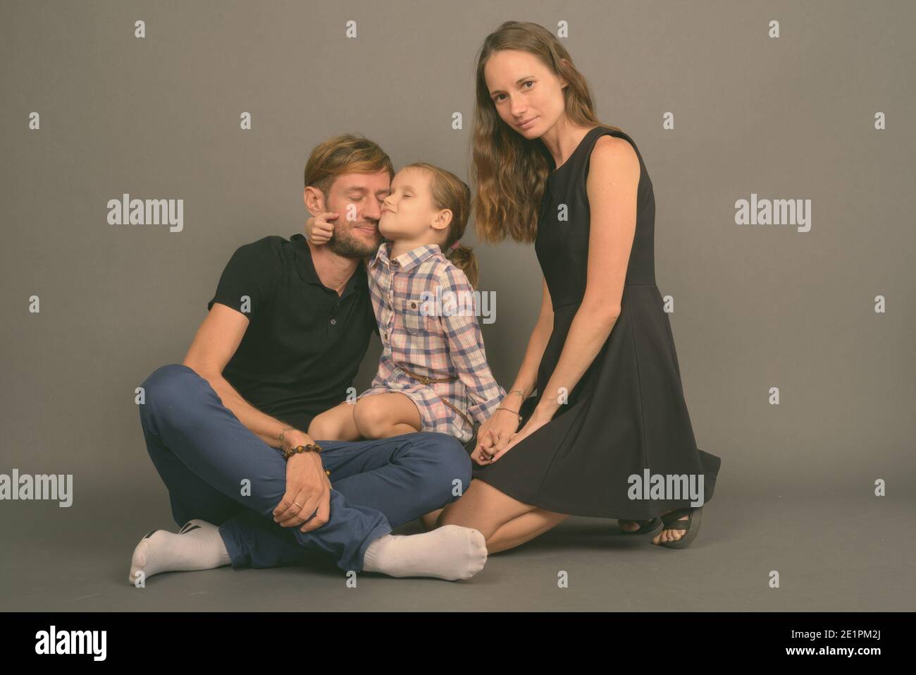 Giovane famiglia felice legare insieme contro lo sfondo grigio Foto Stock