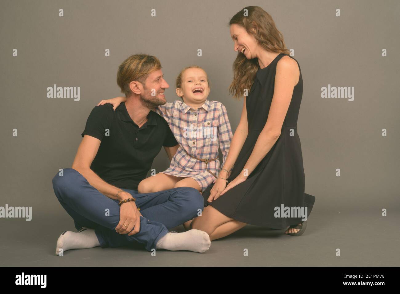 Giovane famiglia felice legare insieme contro lo sfondo grigio Foto Stock