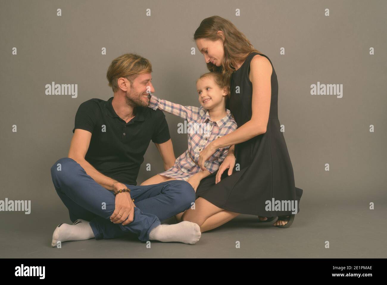 Giovane famiglia felice legare insieme contro lo sfondo grigio Foto Stock