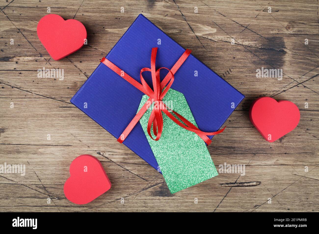 confezione regalo blu con nastro rosso, etichetta regalo vuota e cuori rossi su sfondo in legno. vista dall'alto piatto Foto Stock