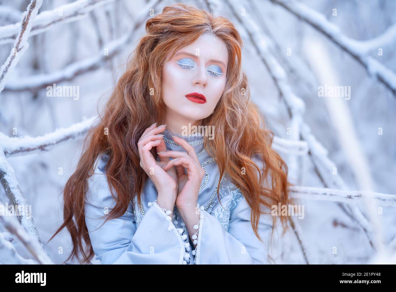 Giovane donna rossa, principessa, cammina in una foresta invernale in un vestito blu. Foto Stock