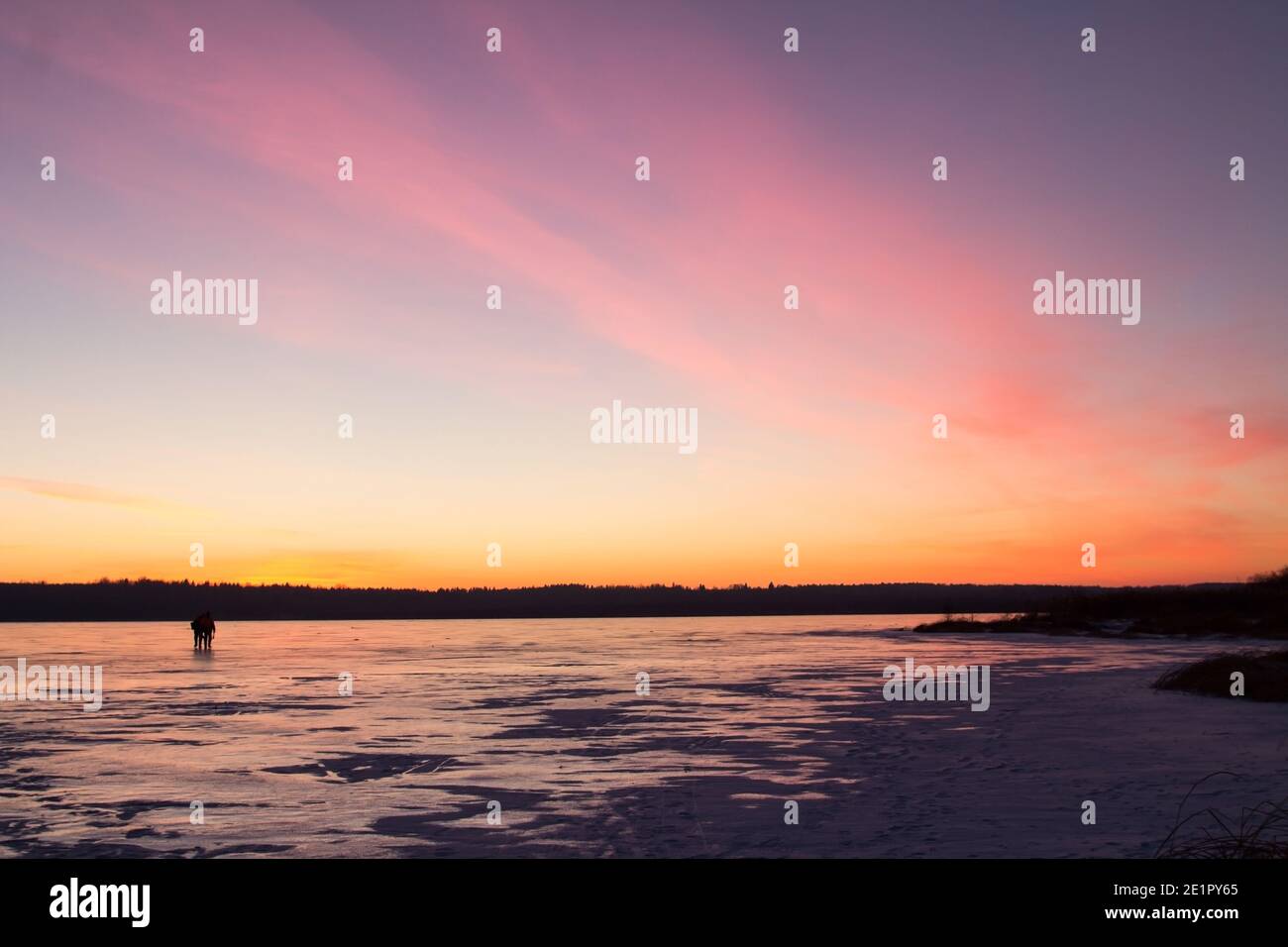 Due sagome di persone sullo sfondo del tramonto sul ghiaccio di un lago ghiacciato. Sfondo invernale. Foto Stock