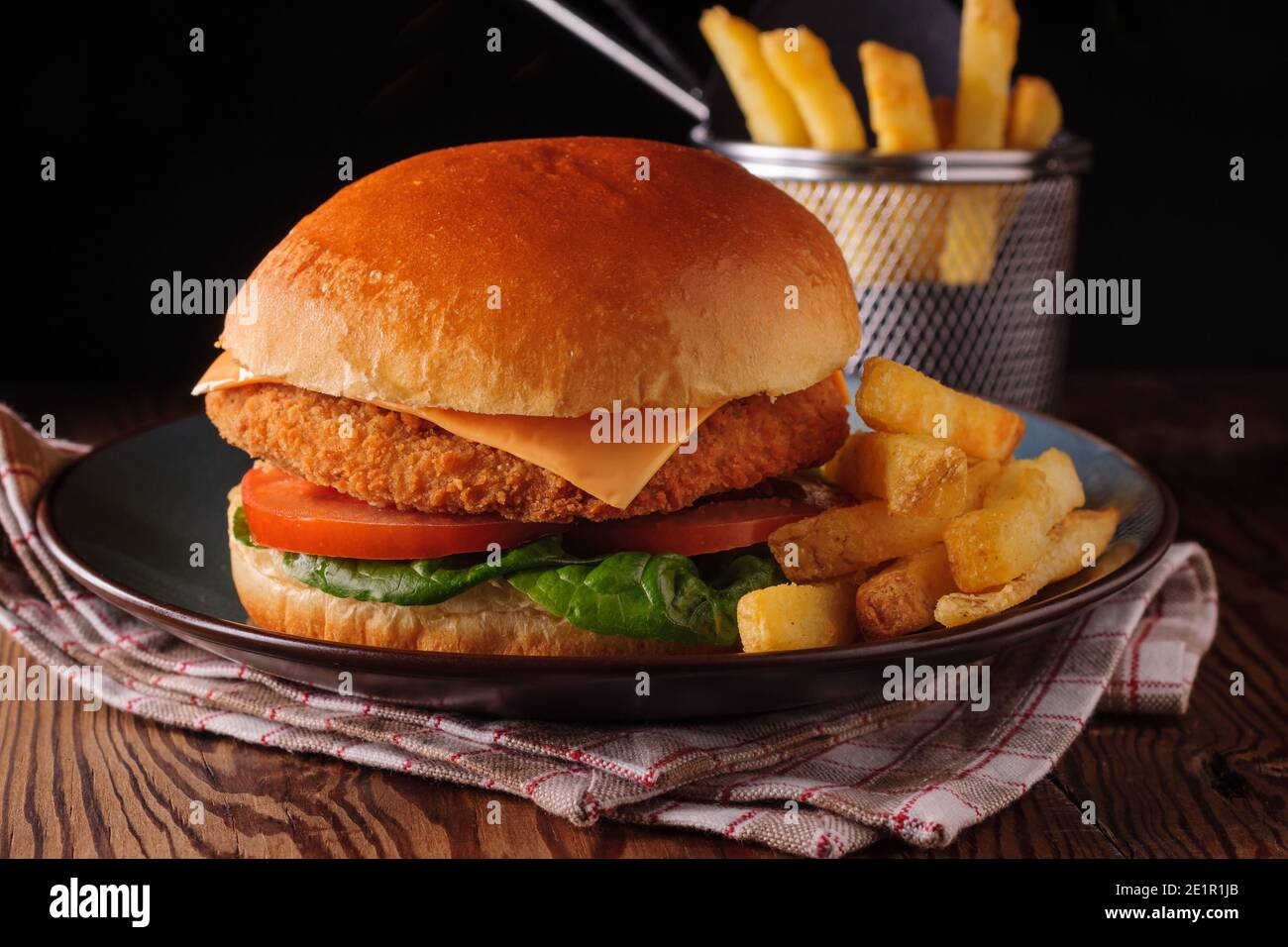 Filetto di pollo in un brioche con lattuga pomodori e formaggio e la pelle su patatine fritte sparate con creatività illuminazione Foto Stock