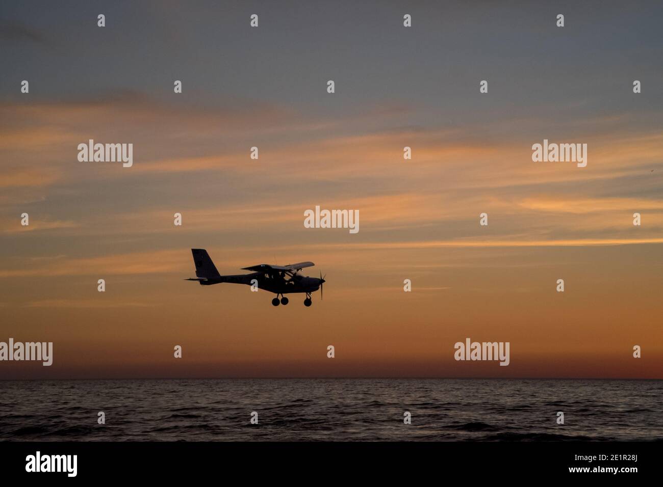 Piccola silhouette di aereo a 2 posti che vola in basso sul Mar Baltico durante tramonto colorato Foto Stock