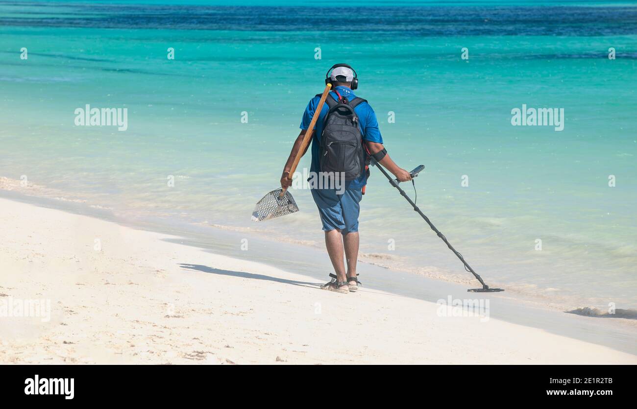 Un uomo cammina sulla spiaggia con un metal detector. Ricerca gioielli e monete. Sullo sfondo il mare dei Caraibi a Playa del Carmen, Messico Foto Stock