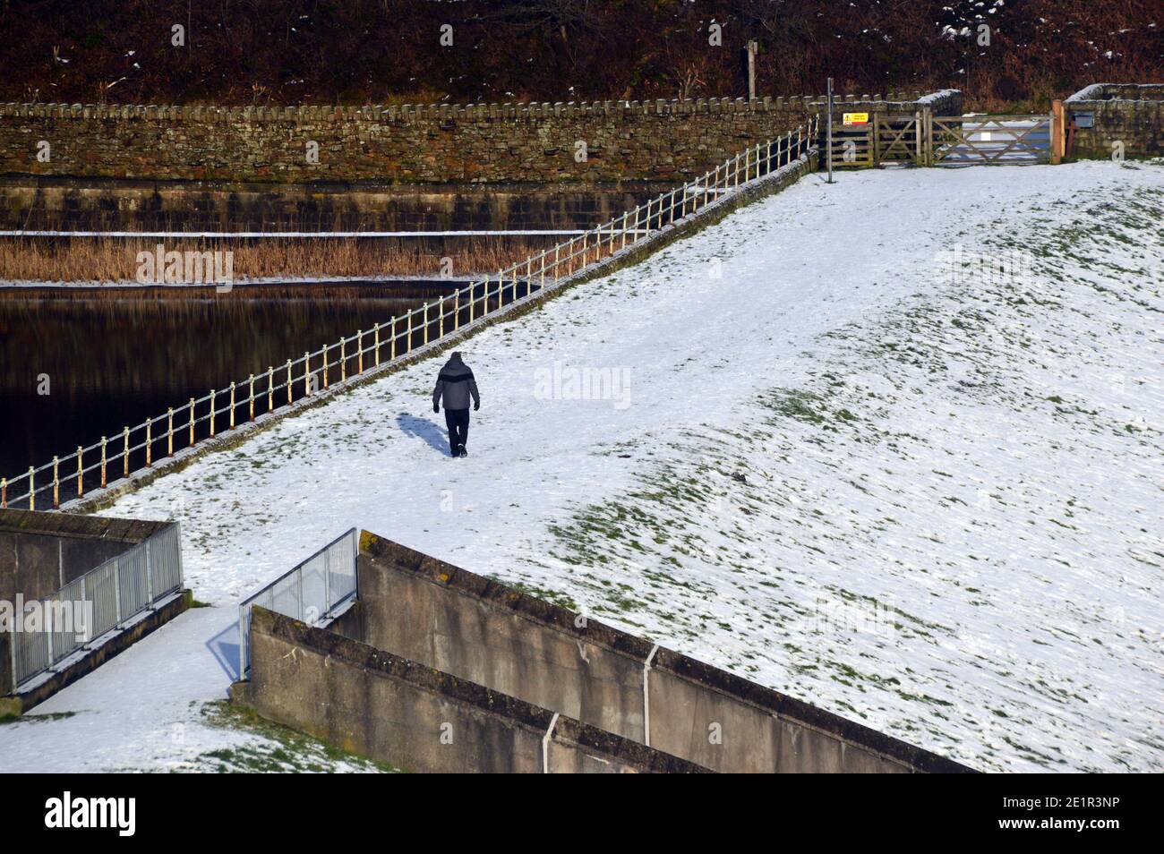Uomo che cammina nella neve sulla diga del lago artificiale di Ogden vicino al villaggio di Barley da Path a Pendle Hill a Ogden Clough, Lancashire. REGNO UNITO. Foto Stock