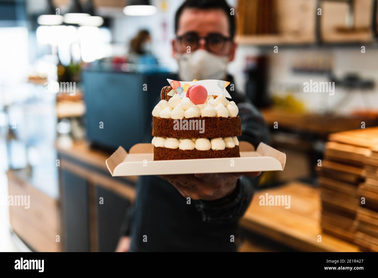 Torta di compleanno tenuta da un panettiere in una panetteria. Il panettiere è fuori fuoco Foto Stock