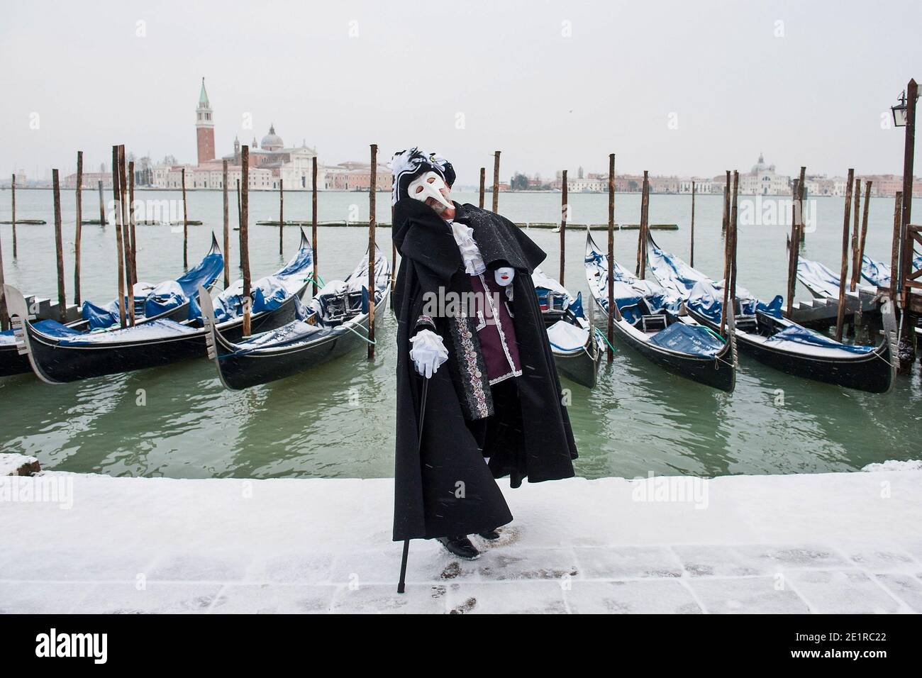 Un uomo che indossa un costume da carnevale davanti alle gondole vestite di neve, Venezia Italia Foto Stock
