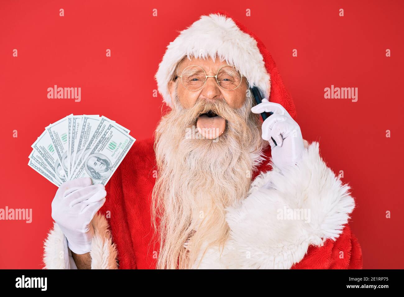 Vecchio uomo anziano che indossa il costume di babbo natale che tiene i  dollari e lo smartphone che attacca la lingua fuori felice con  l'espressione divertente Foto stock - Alamy
