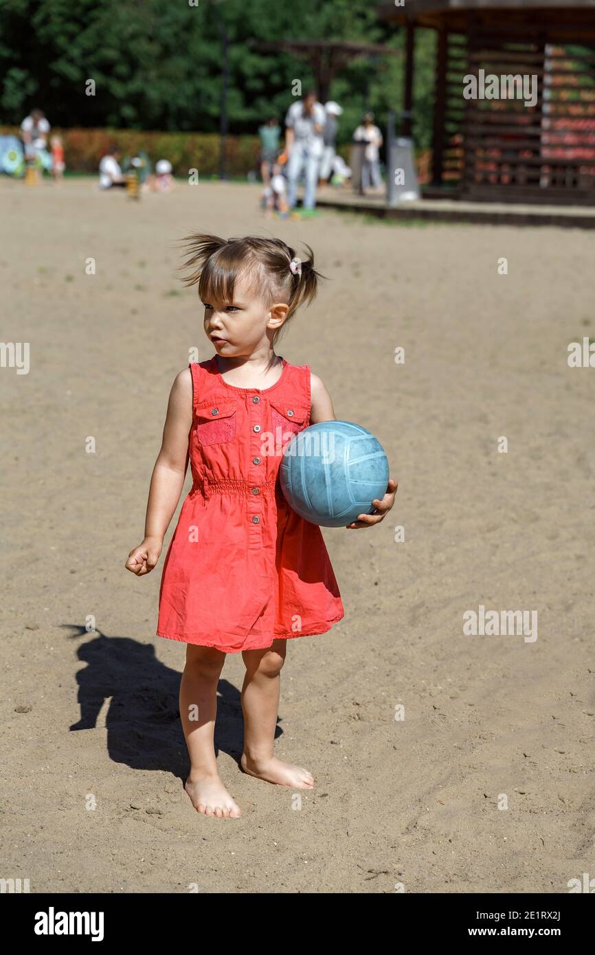 bella bambina in un vestito rosso e a piedi nudi con una palla in un parco  cittadino Foto stock - Alamy