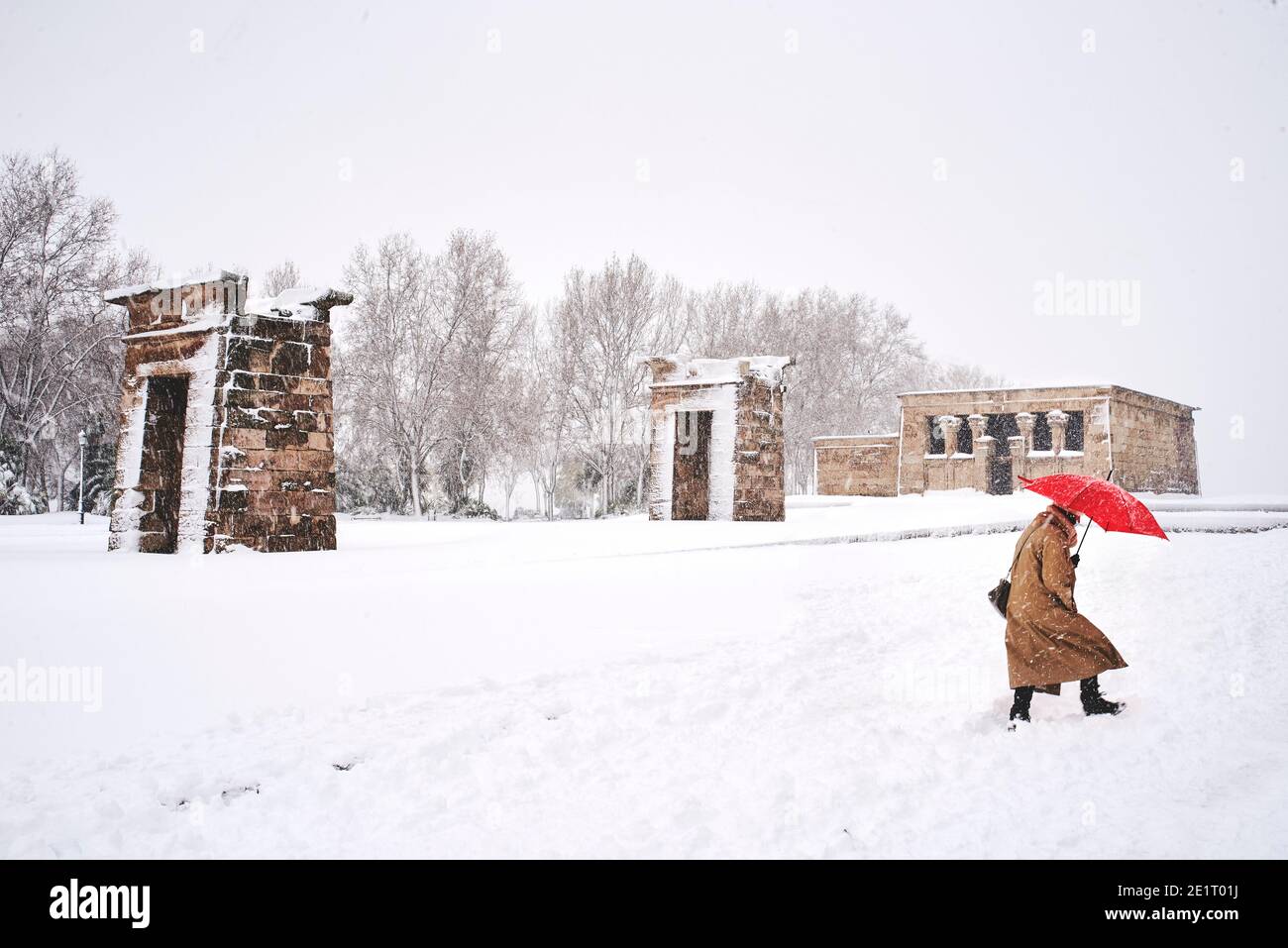 Una donna con un ombrello rosso che attraversa il Parco Cuartel de la Montana in mezzo alla bizzarda con il Tempio di Debod sullo sfondo. Madrid, Spagna. Foto Stock