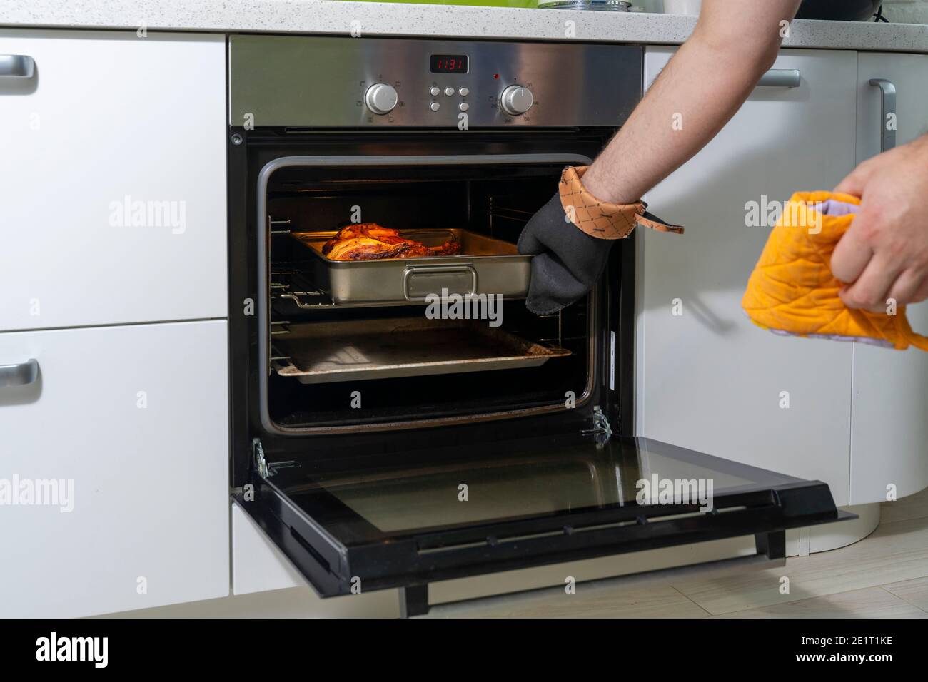 un uomo in guanti resistenti al calore toglie un pollo cotto del forno Foto Stock