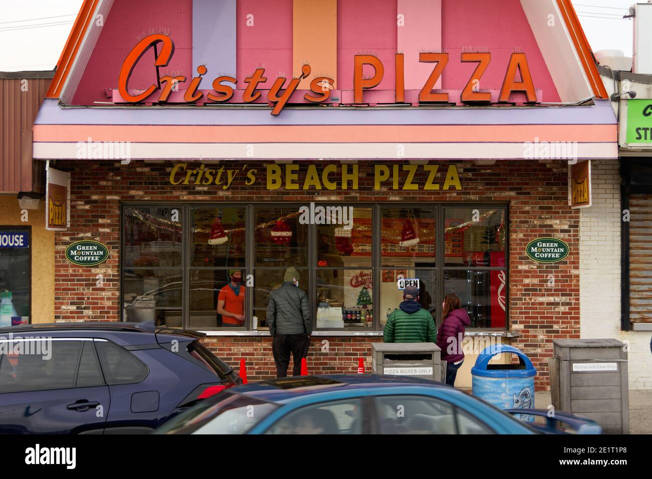Salisbury Beach, Massachusetts - UN negozio di pizza dai colori vivaci sul lungomare con il server e i clienti che indossano maschere e outerwear invernale su un Foto Stock