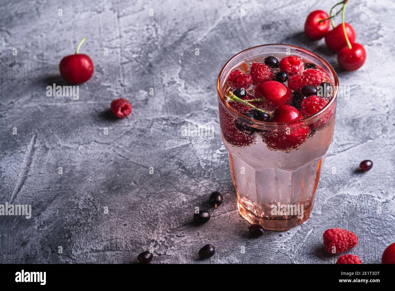 Bevanda fresca fredda con ciliegia, lampone e ribes in vetro rosso sfaccettato su fondo di pietra in cemento, dieta estiva, A. Foto Stock