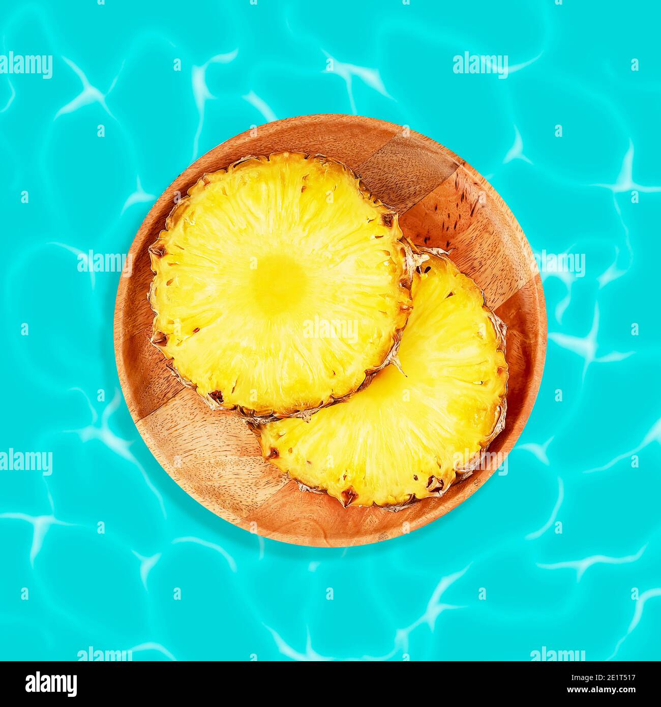 Fette rotonde di ananas su un piatto di legno su fondo blu d'acqua. Il concetto di un cibo sano per la perdita di peso. Cibo esotico per rilassarsi. Ananas Foto Stock