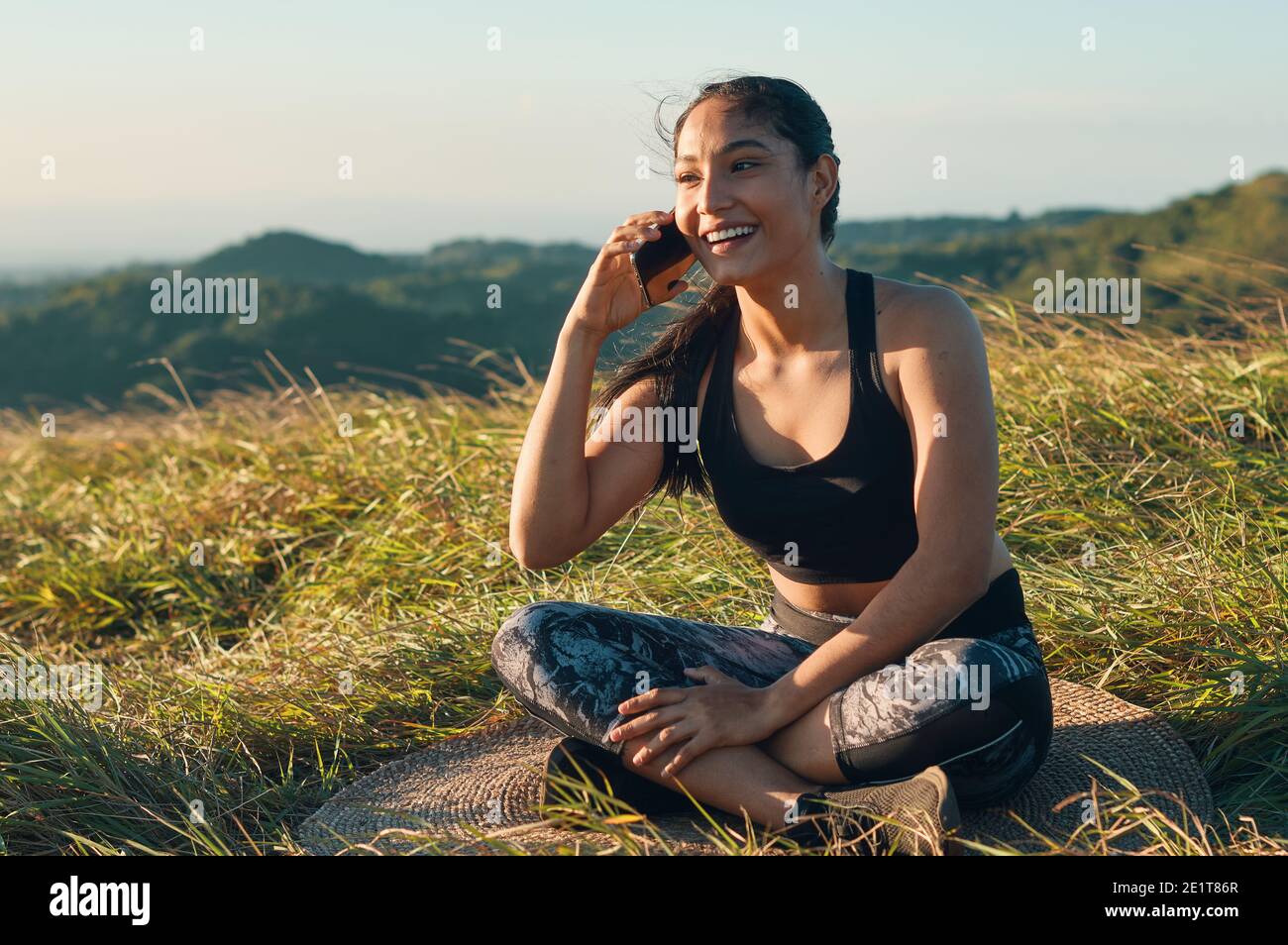 Una giovane donna in forma che riposa dopo l'addestramento all'aperto che parla sopra un telefono cellulare Foto Stock