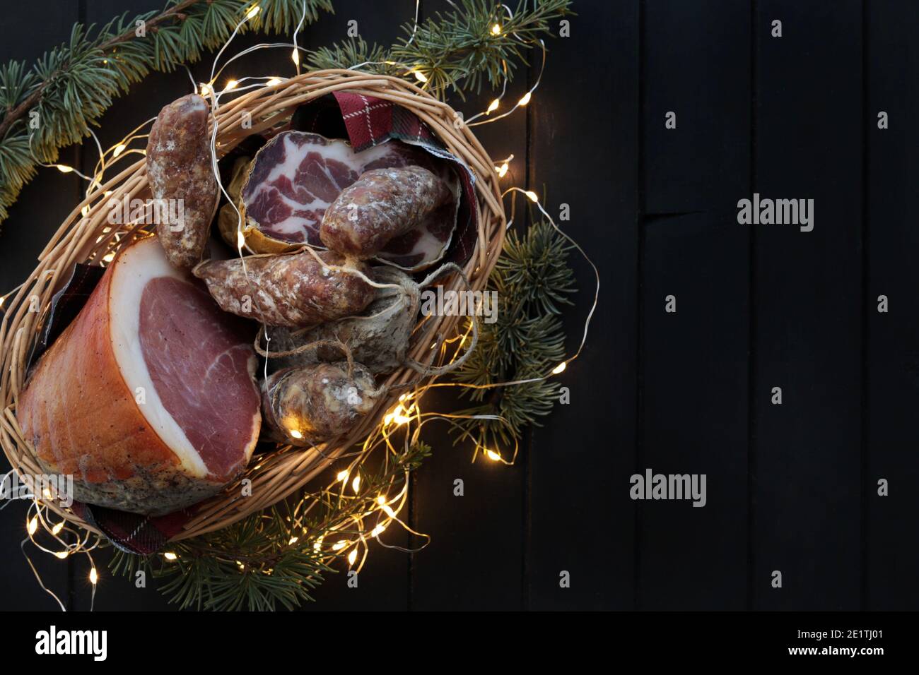 Cesto con salame, coppa e prosciutto su fondo di legno scuro. Specialità italiane. Decorazioni natalizie. Foto Stock