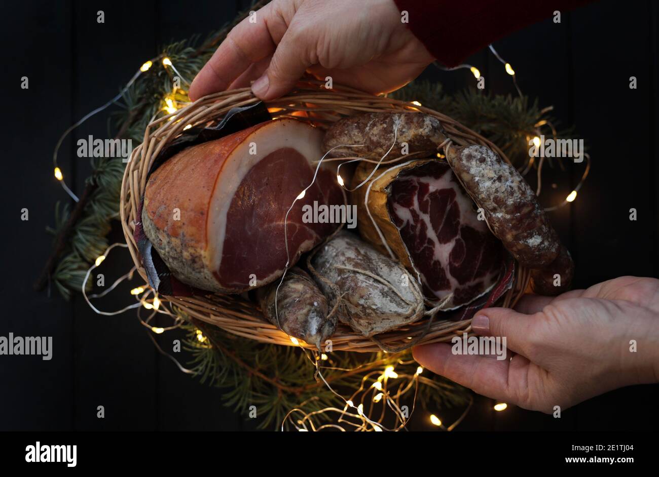 Cesto con salame, coppa e prosciutto su fondo di legno scuro. Specialità italiane. Decorazioni natalizie. Foto Stock