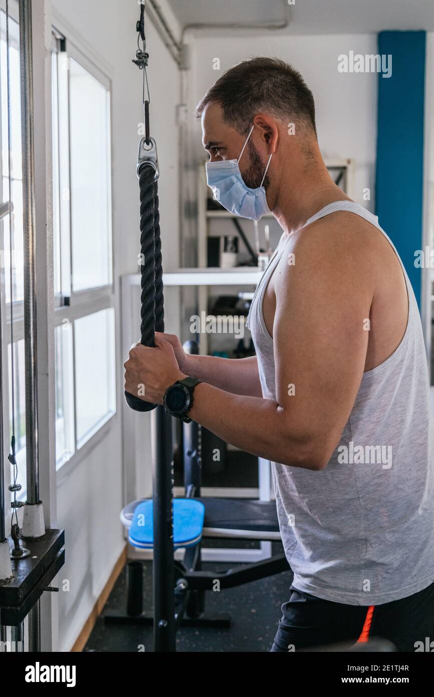 Uomo in palestra con una maschera che fa tricipiti con corde. Covid19. Coronavirus Foto Stock