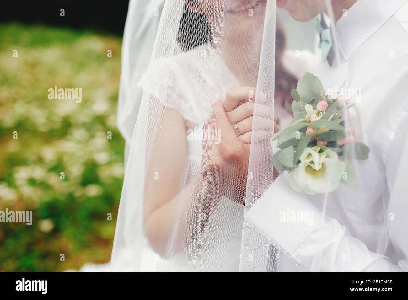 Sposo in camicia bianca con cravatta e boutonnière tiene la sposa mano sotto velo Foto Stock