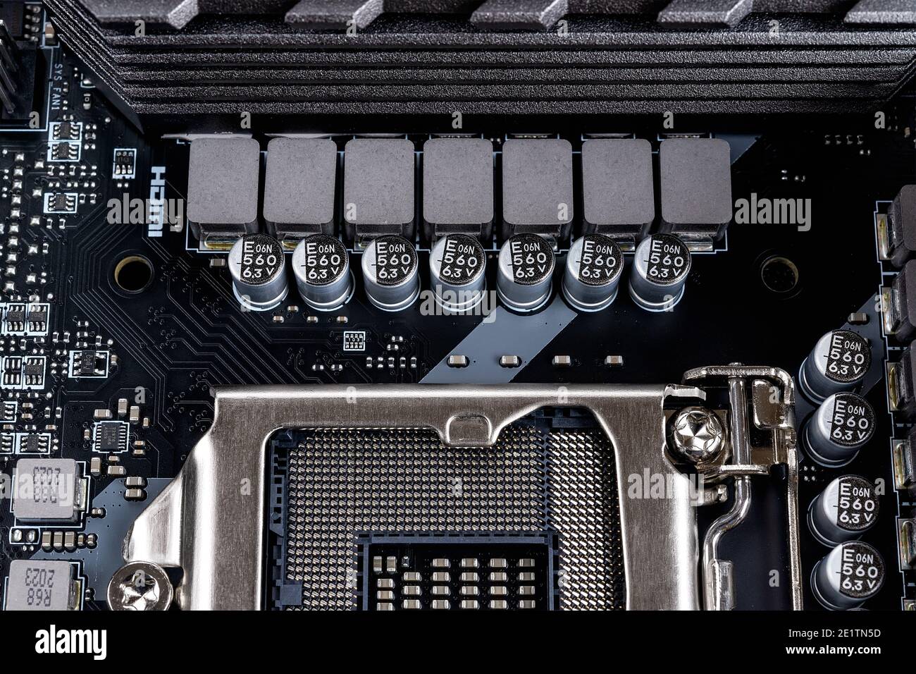 Induttori e condensatori per socket cpu che alimentano una moderna scheda madre nera. Componenti del circuito della scheda madre del calcolatore. Macro hardware desktop. Foto Stock