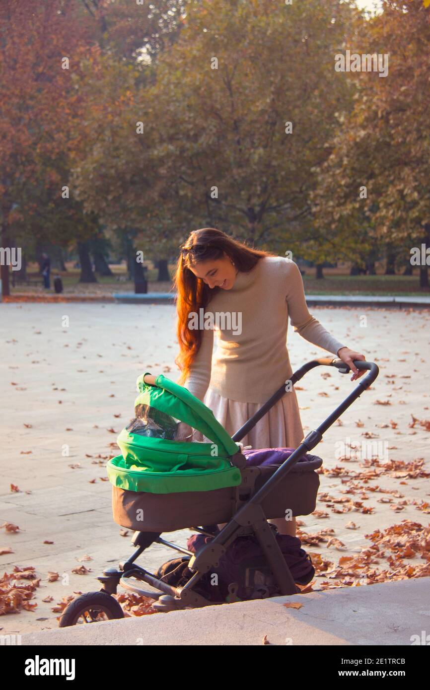 La giovane madre è fuori nel parco con lei bambino per una passeggiata con il pram su un bello giorno d'autunno Foto Stock