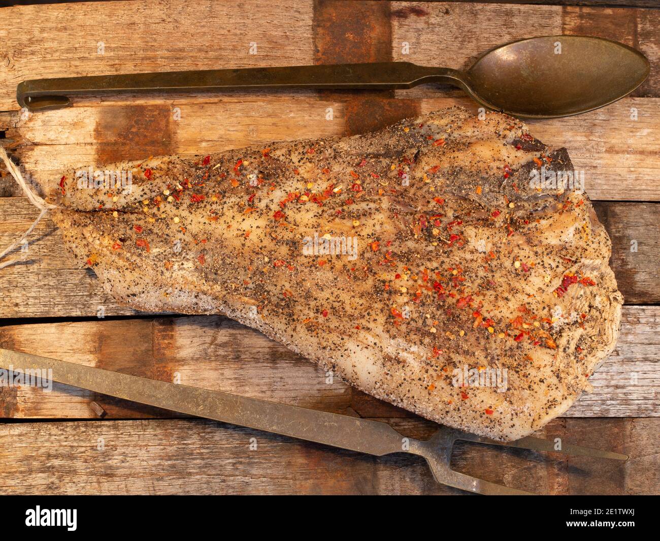 guanciale italiano guanciano su tavola di legno. ingrediente principale per carbonara e matriciana con posate vecchie su tavola di legno con cucchiai e forchette. Foto Stock