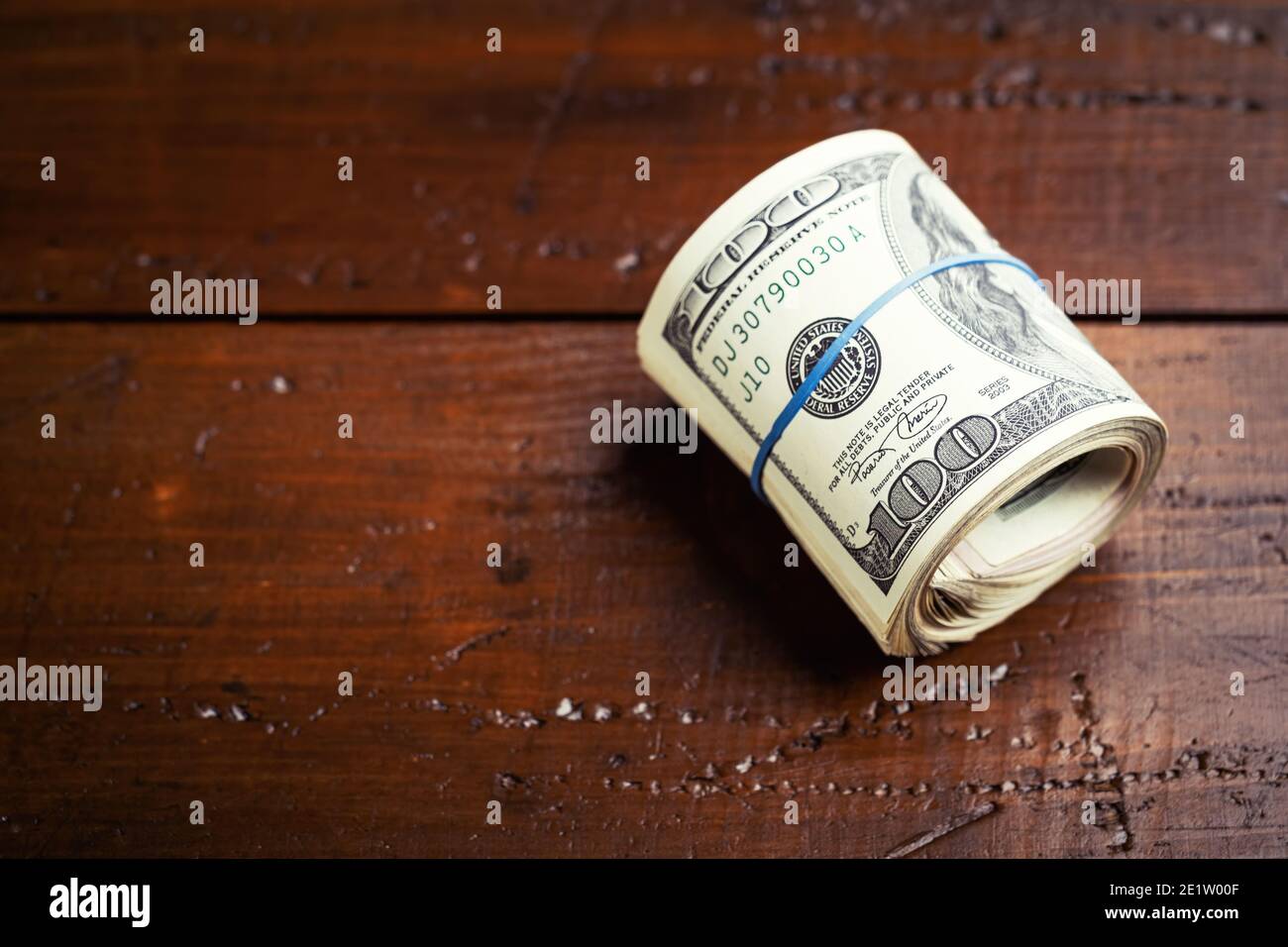 Rotolo di denaro con gomma su tavola di legno - cento banconote USA con ritratto del presidente Franklin. Contanti di cento fatture del dollaro, valuta della carta ba Foto Stock