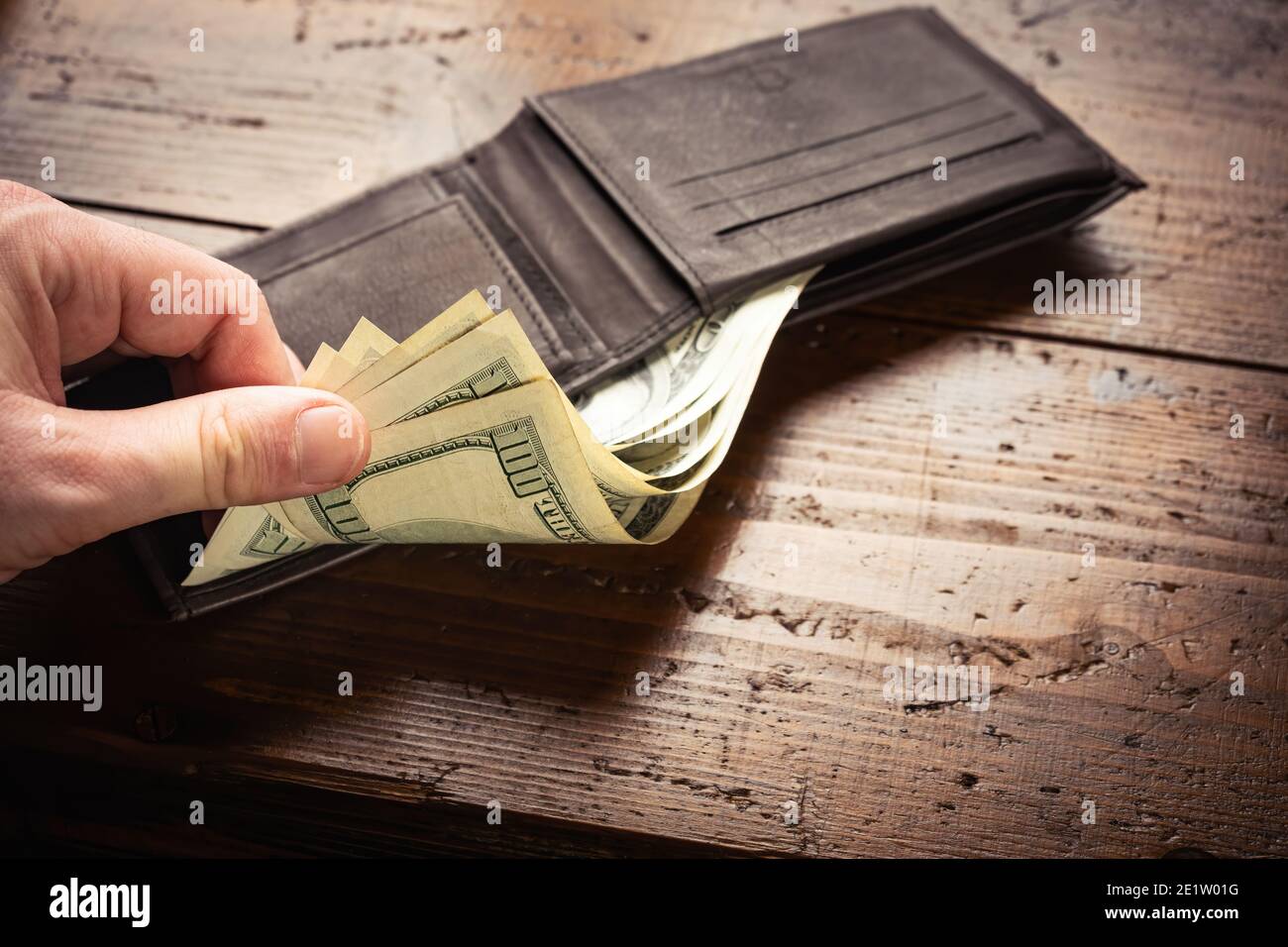 Mano che preleva i soldi da cento banconote americane in portafoglio di pelle su sfondo di tavola di legno. Contanti di cento fatture del dollaro, valuta di soldi della carta. Foto Stock