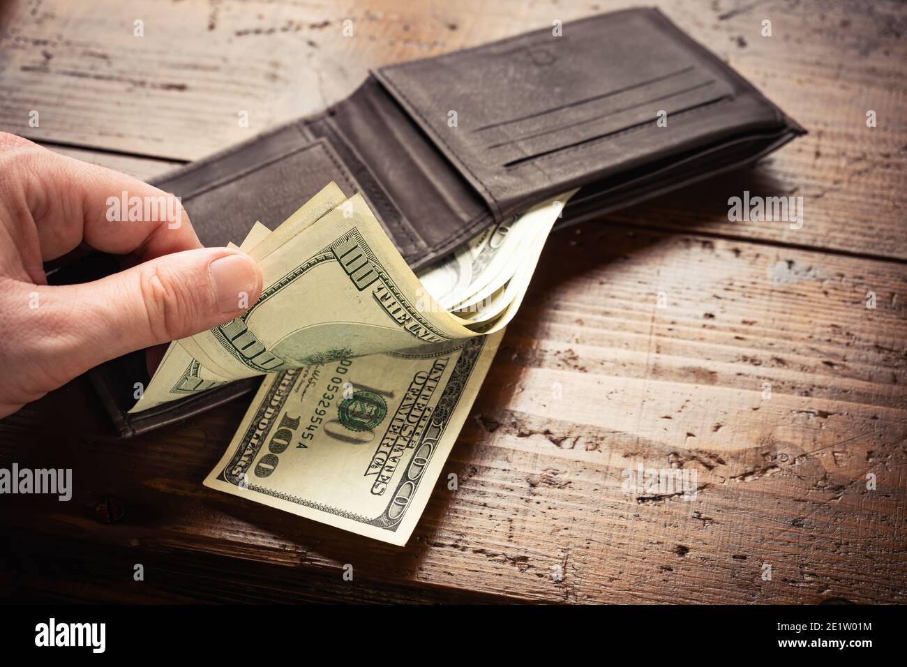 Mano che preleva i soldi da cento banconote americane in portafoglio di pelle su sfondo di tavola di legno. Contanti di cento fatture del dollaro, valuta di soldi della carta. Foto Stock