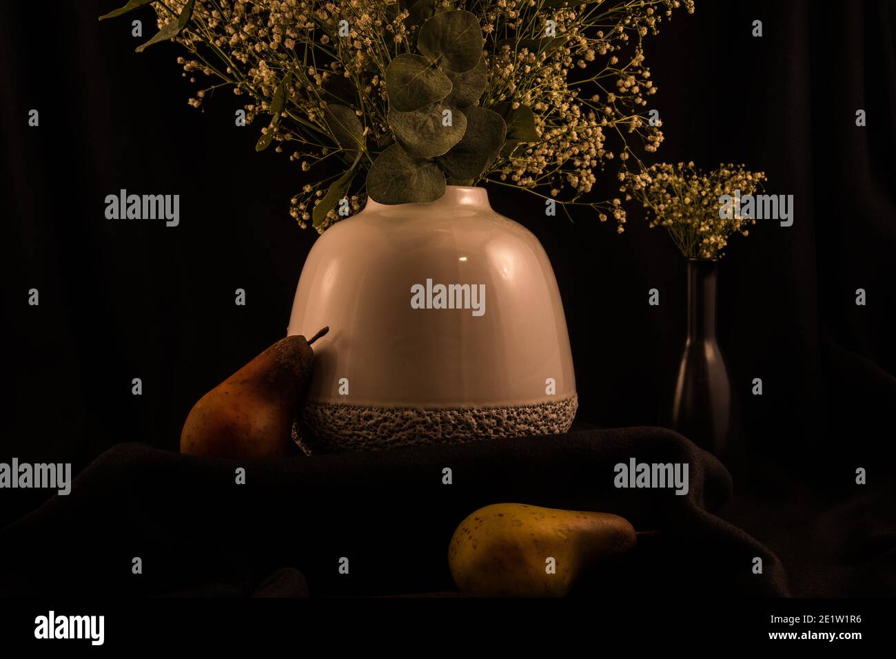Vaso bianco morbido con fiori 'baby's breath' su sfondo scuro, frutta artificiale aggiunge un bel tocco. Foto Stock