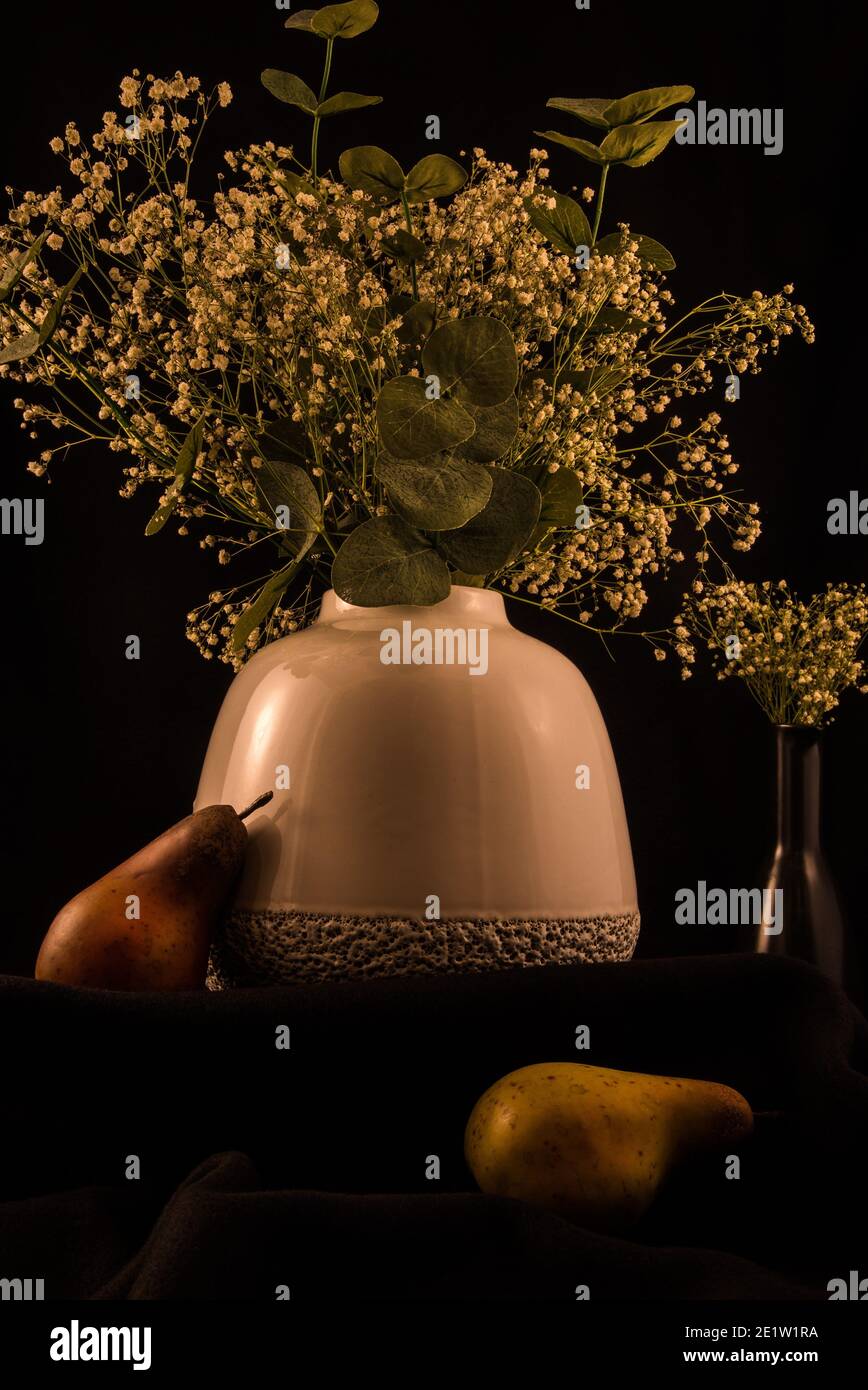 Vaso bianco morbido con fiori 'baby's breath' su sfondo scuro, frutta artificiale aggiunge un bel tocco. Foto Stock