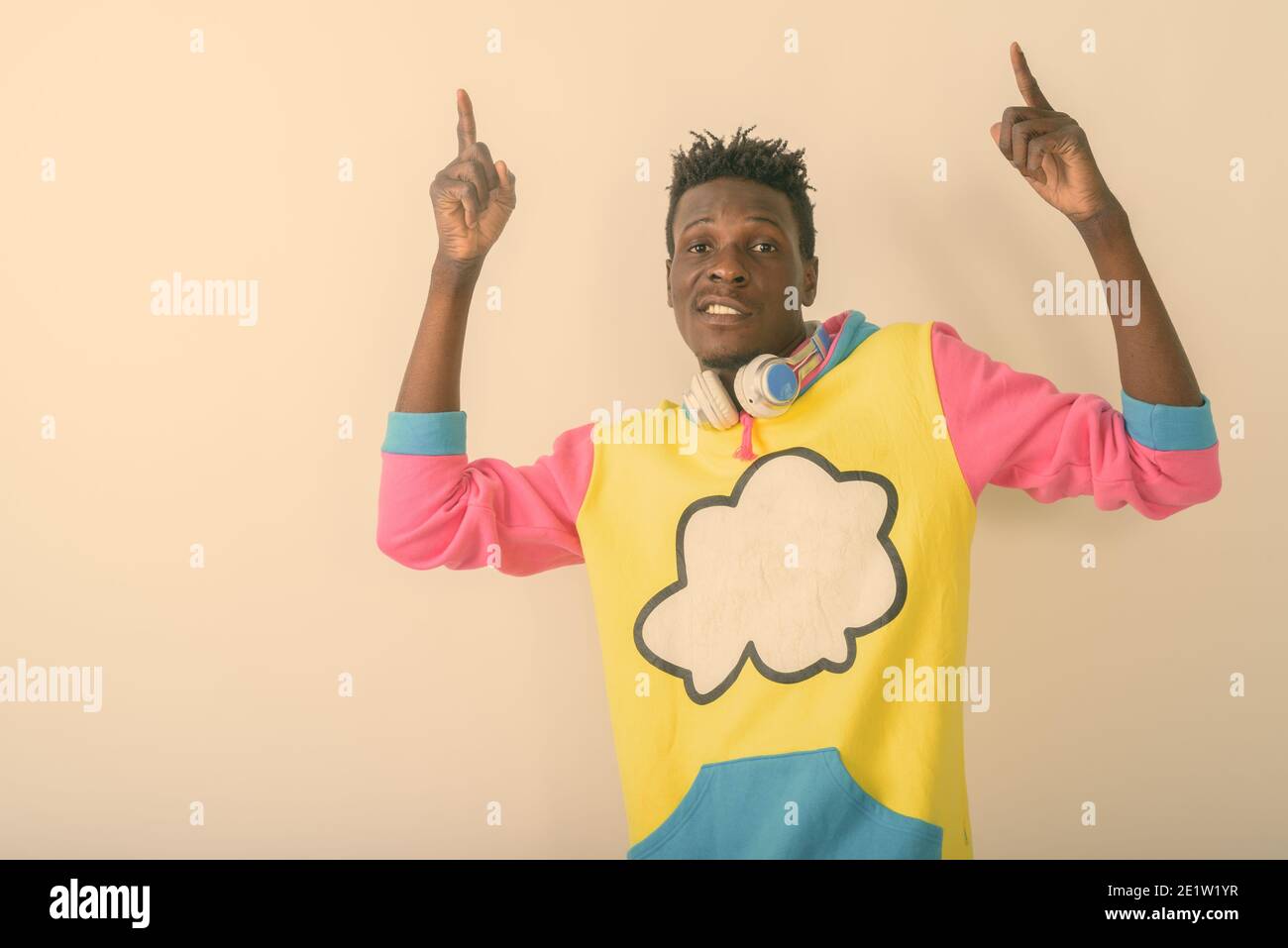 Studio shot del giovane nero africano puntando entrambe le dita verso l'alto mentre posa con cuffie attorno al collo contro uno sfondo bianco Foto Stock