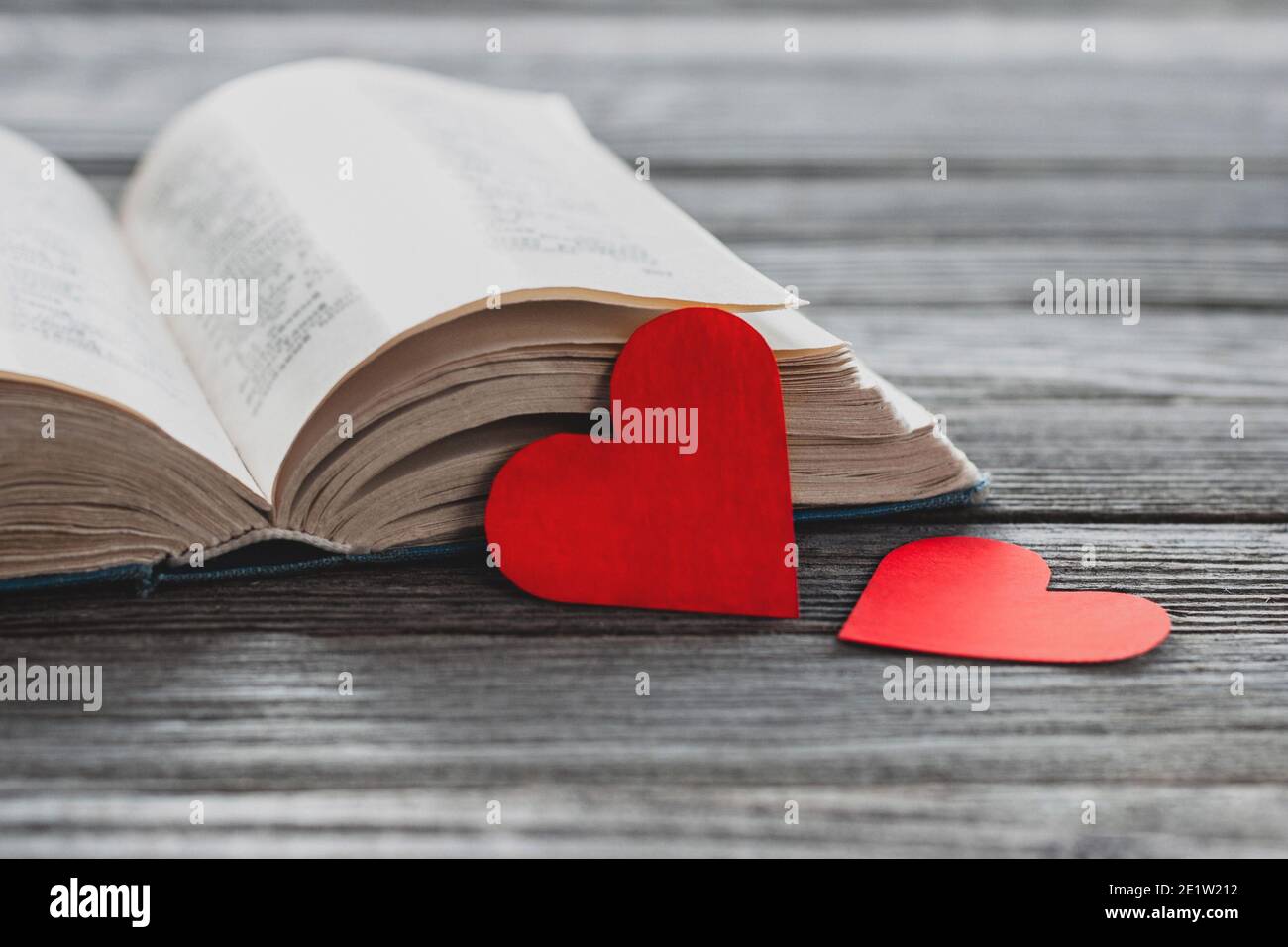 due cuori di carta rossa e libro aperto su tavola di legno Foto Stock