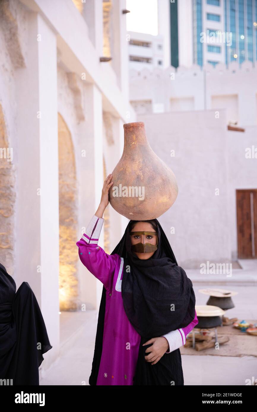 Signora Emarati in abiti tradizionali che tiene un vaso su di lei fai un giro della casa Foto Stock