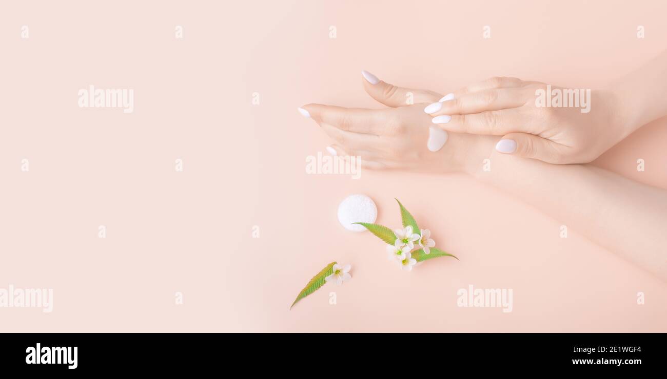 mani con crema su fondo rosa con fiori bianchi di mela primo piano. prodotto per la cura della pelle, bellezza, cura delle mani, spa. Foto Stock