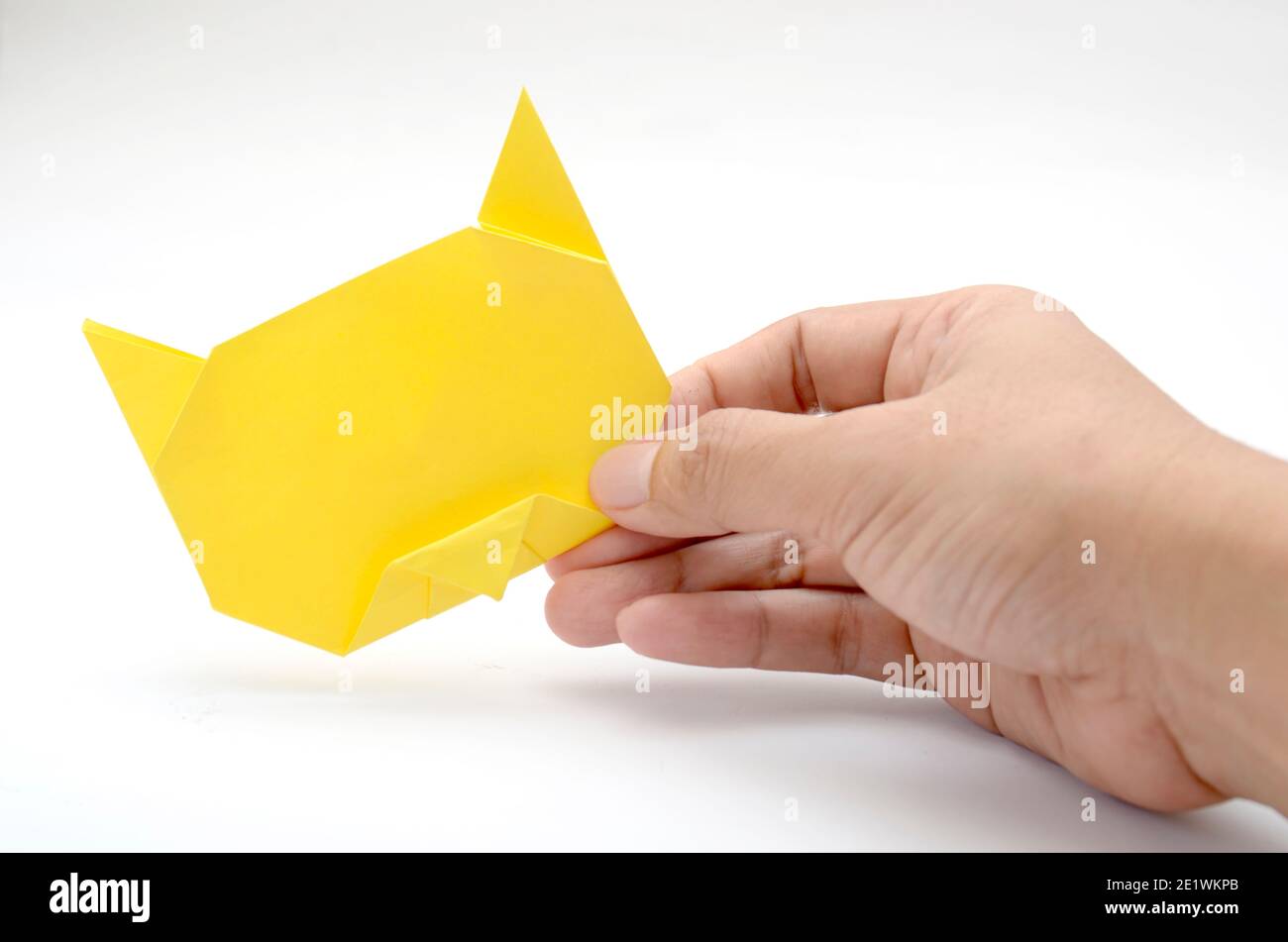 mano che tiene carta gialla, origami testa di gatto. Sfondo bianco Foto Stock